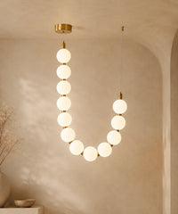 Suspension luminaire perles, un brin en U à connecteurs dorés, allumée sur fond beige