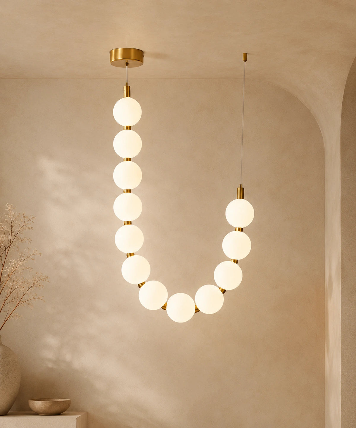Suspension luminaire perles, un brin en U à connecteurs dorés, allumée sur fond beige