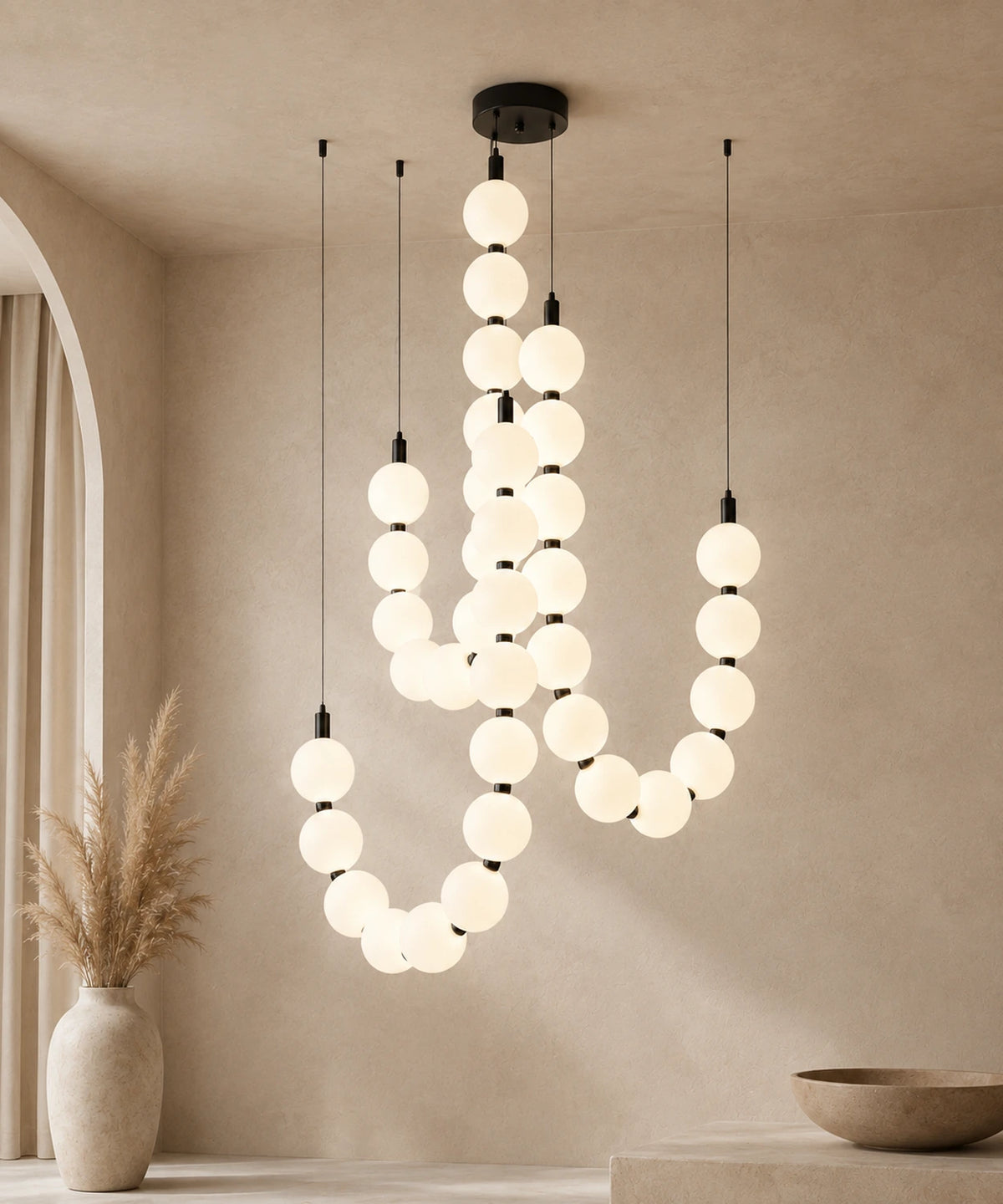Suspension luminaire perles à trois brins, connecteurs noirs, allumée sur fond beige