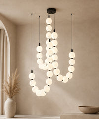 Suspension luminaire perles à trois brins, connecteurs noirs, allumée sur fond beige
