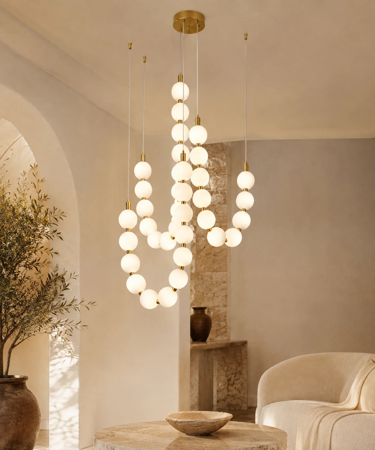 Suspension luminaire perles à trois brins dorés allumée dans un salon aux murs enduits