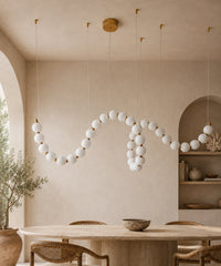 Suspension à boules opalines à connecteurs dorés, 150 cm, allumée au-dessus d’une table