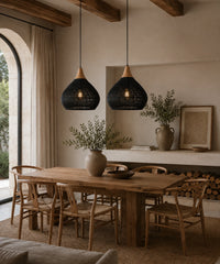 Deux suspensions luminaire rotin noir et bois au-dessus d’une table à manger en bois brut