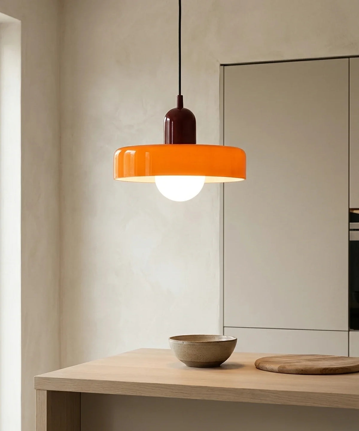 Suspension en verre coloré orange allumée au-dessus d’un plan de travail en chêne