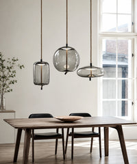 Suspension luminaire verre soufflé, cylindre et galet fumés suspendus devant de grandes fenêtres