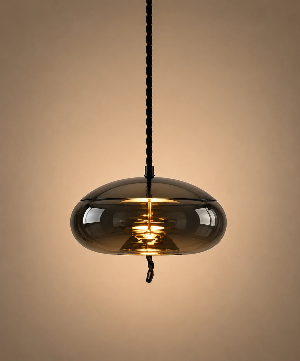 Suspension en verre soufflé fumé en forme de galet aplati, allumée sur fond beige