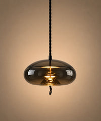 Suspension en verre soufflé fumé en forme de galet aplati, allumée sur fond beige