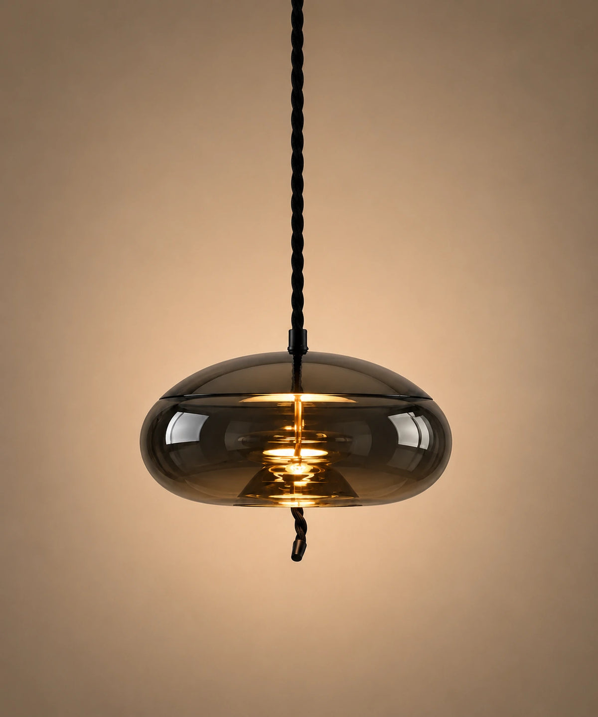 Suspension en verre soufflé fumé en forme de galet aplati, allumée sur fond beige