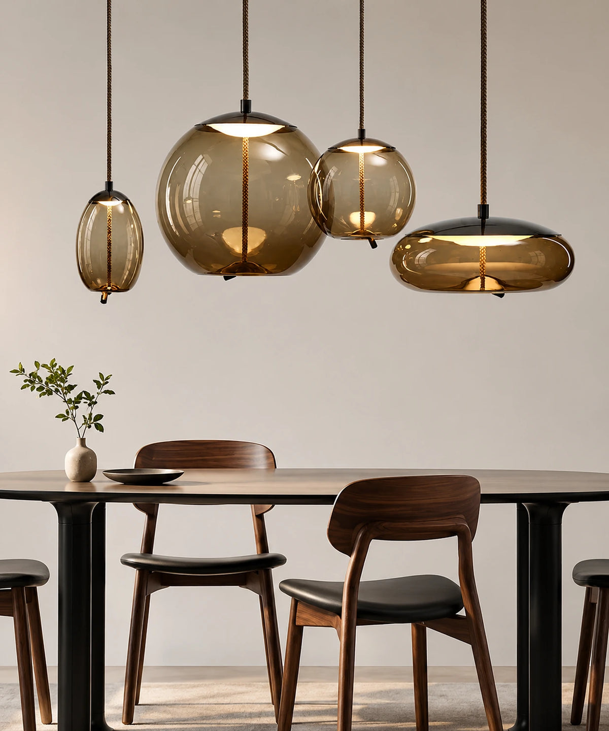 Suspension luminaire en verre soufflé, quatre globes cognac et fumé allumés au-dessus d’une table à manger