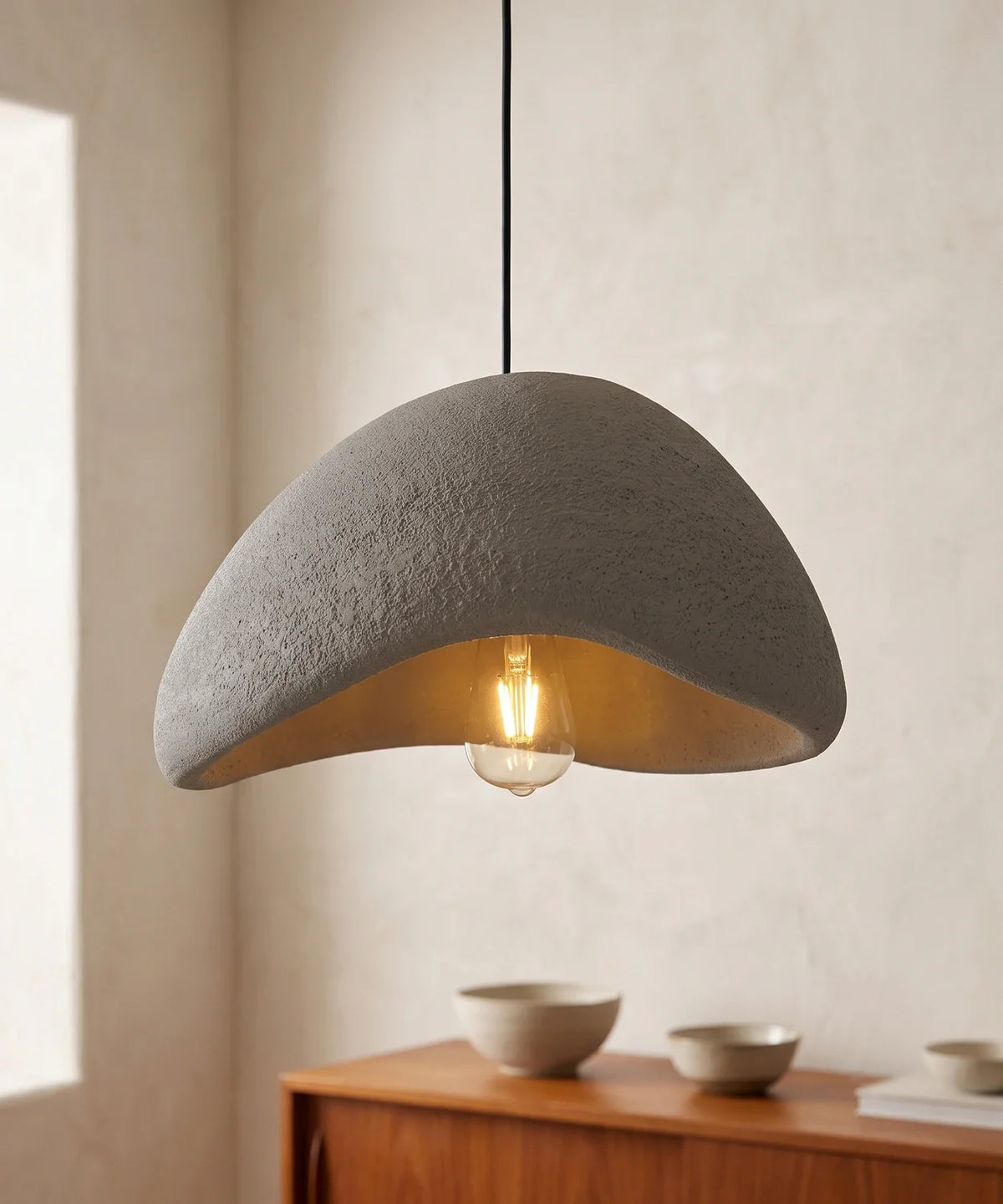 Suspension wabi sabi galet grise coque ouverte allumée au-dessus d un buffet en noyer