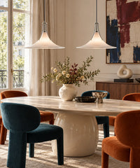 Deux suspensions en verre blanc et chrome au-dessus d’une table ovale avec chaises bleu et orange
